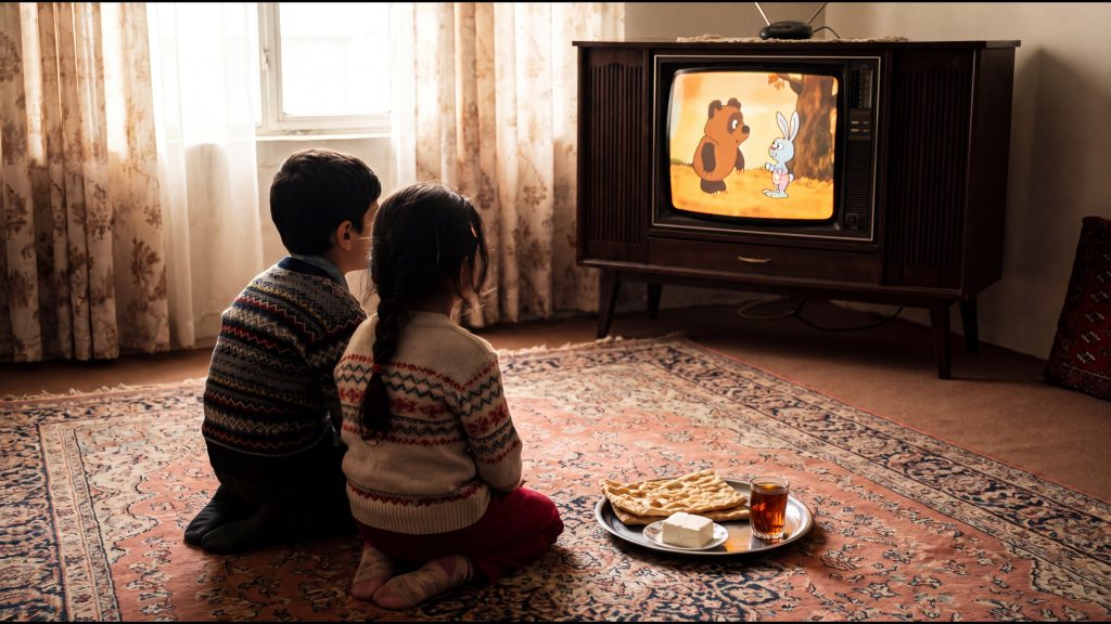 بچه‌های دهه شصت روی فرش جلوی تلویزیون قدیمی در حال تماشای کارتون صبح جمعه